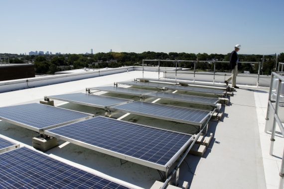 Solar panels on the roof of Sophia Gordon Hall, with man observing with helmet on