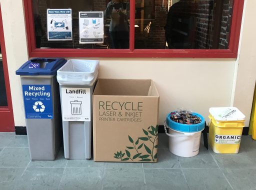 A waste station on the Medford/Somerville campus with regular, battery, and ink and toner recycling bins and a composting bin