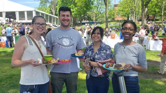 Four people stand holding reusable utensils at an outdoor lunch