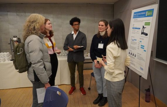 Five students standing in a circle discussing a project at the event.