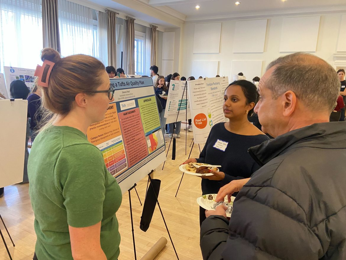 Simran Patel discusses her air quality research poster with symposium attendees at the ENVS event, with her presentation board clearly showing 'Developing a Tufts Air Quality Plan' and colorful charts and information.