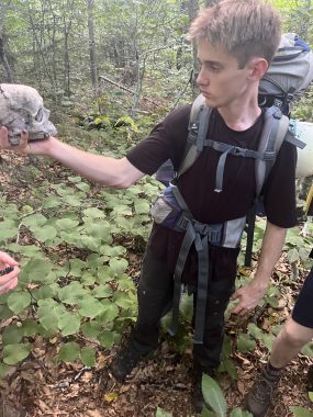 Connor standing in a forest inspecting a human skull artifact.