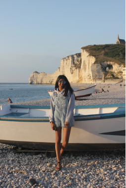 Girl standing in front of a boat on a beach with cliffs in the background