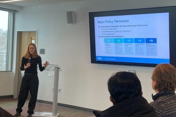 A student stands at the front of the room presenting on her work on scope 3 carbon emissions.