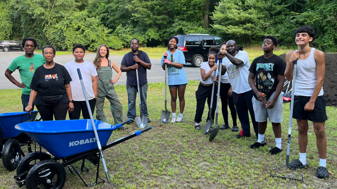 A group of people pose with garden tools while building a new community garden in Brockton, MA