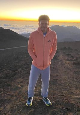 Marlon standing on a mountaintop with the sun in the horizon.