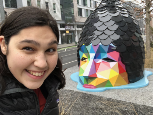 Close-up of a girl smiling with a multi-colored sculptural head in the background