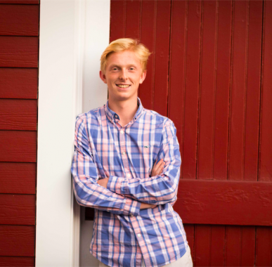 Tom standing with his arms crossed in front of a red barn.