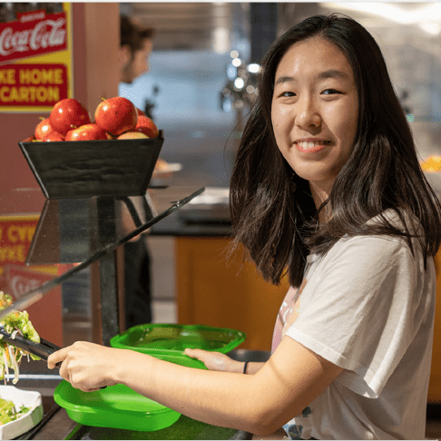 Girl getting food at a dining hall, using a reusable container