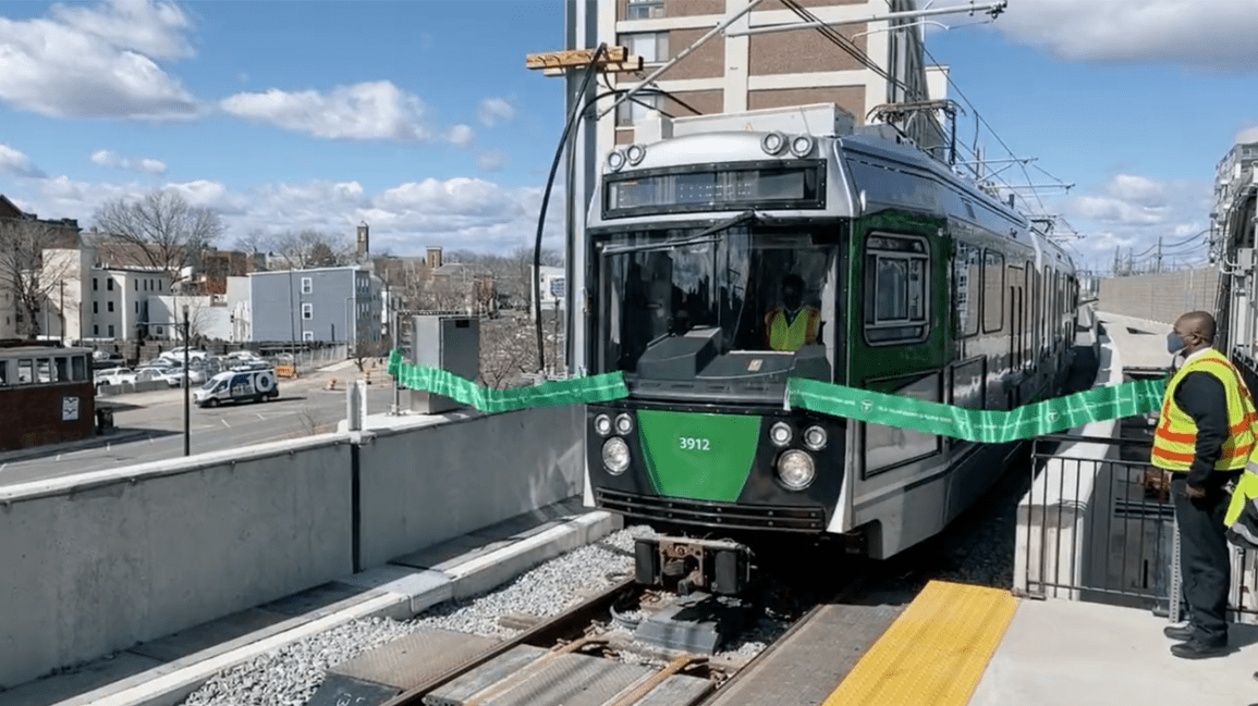 A green line train breaks through a green ribbon outside